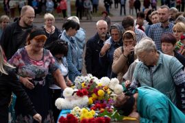 People paying their respects to a Ukrainian soldier killed in the war. There are flowers on the coffin. People are standing around it. Many are weeping. One woman has bent over to put her face to the coffin