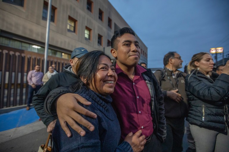 A man wraps his arm around an older female family member, who smiles with anticipation. The photo depicts members of Alina Narciso's family waiting for her release outside the La Mesa prison in Tijuana in May 2023.