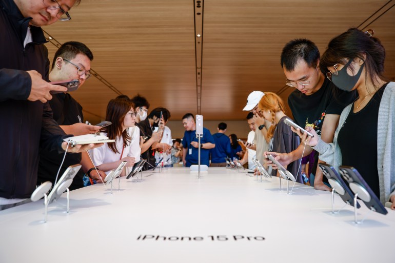 People in Beijing looking at the new iPhone 15 in the Apple store. They are standing along either side of a long white table.