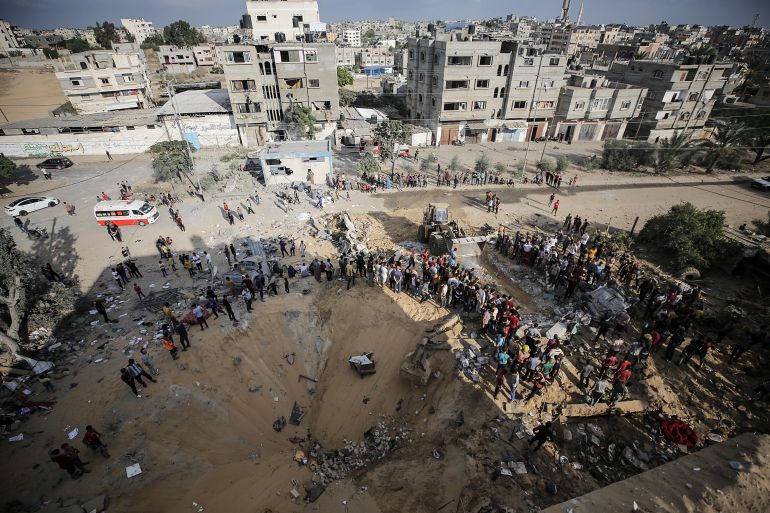Palestinians stand next to a crater caused by an explosion from an Israeli airstrike