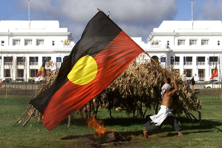 An Aboriginal protester runs past a fire and make-shift shelter with an Aboriginal flag outside the old parliament House building in Canberra