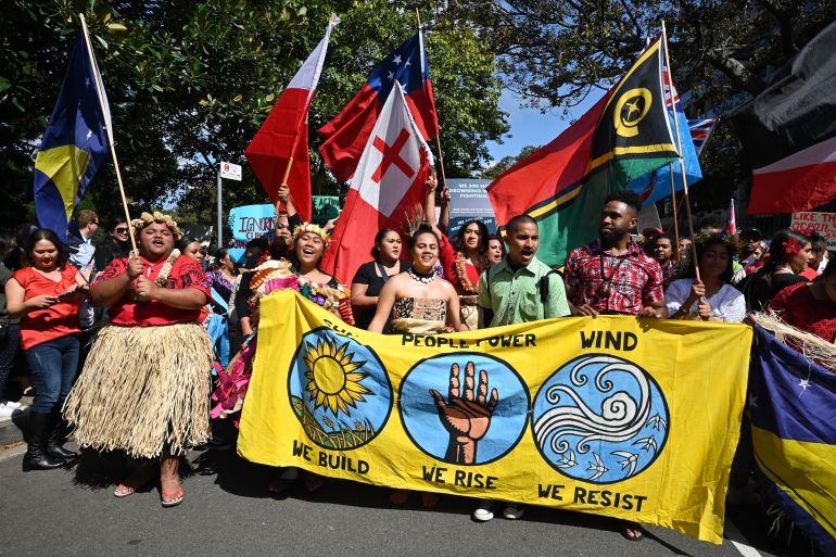 Pacific islanders protesting at a climate rally in Sydney. They are carrying flags and a large banner reading: sun, people power, wind