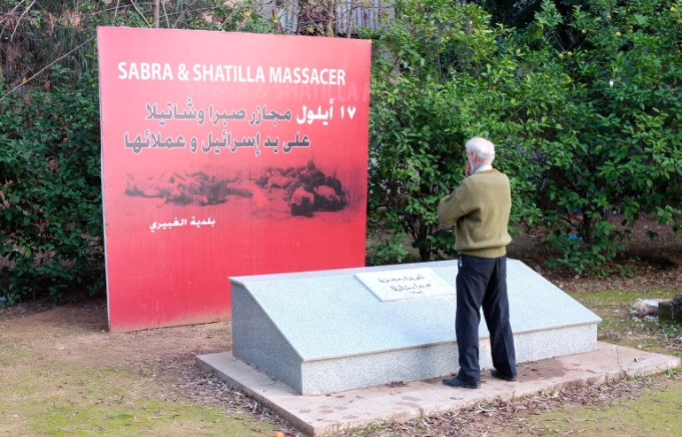 Yousef Hamzeh, a white-haired man seen from behind, stands at a granite memorial. Behind it is a red sign that reads 