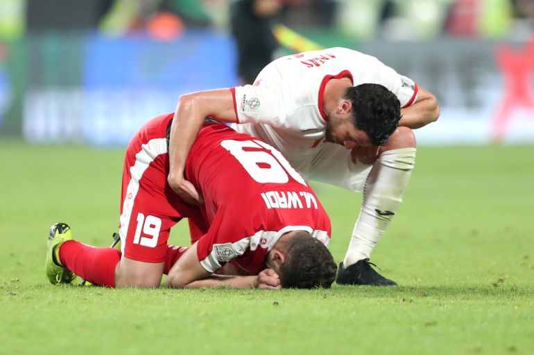 Palestine's Mahmoud Wadi sinks to the floor and folds over, while comforted by a Jordanian player