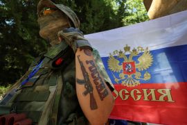 A participant stands next to a Russian state flag at an exhibition showcasing volunteers' product range, manufactured to supply the needs of service members involved in Russia's military campaign in Ukraine, in Yevpatoriya, Crimea, July 29, 2023. A tattoo reads: "Russia". REUTERS/Alexey Pavlishak