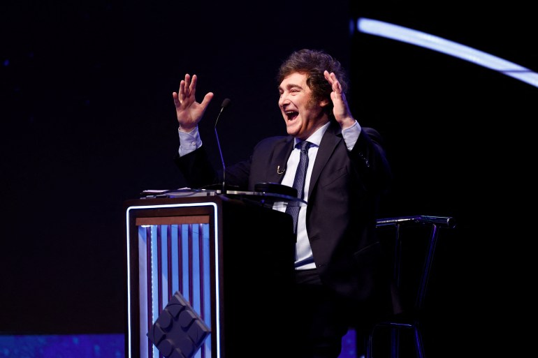 Argentine presidential candidate Javier Milei stands behind a podium on the debate stage, his hands in the air, mid-gesture. 