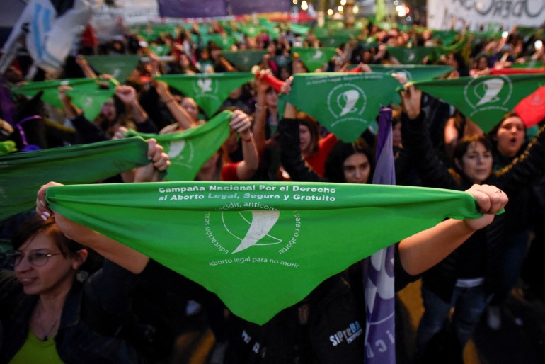 A large group of protesters hold above their heads green bandanas, a symbol of abortion rights.
