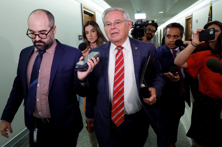 Senator Robert Menendez walks down the halls of Congress with a trail of reporters around him, holding out phones, cameras and other recording devices.