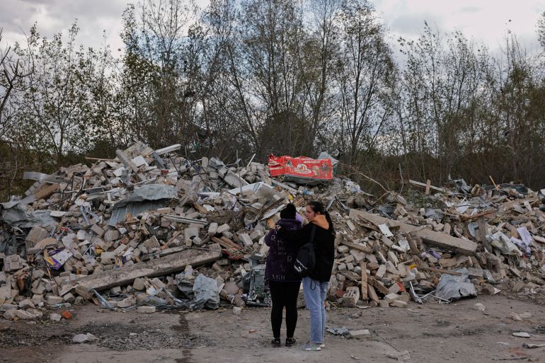 Two women react in front of a pile of rubble that is left of the cafe that hosted the wake and was hit by a Russian missile