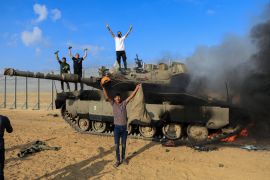 Palestinians celebrate as an Israeli military vehicle burns after it was hit by Palestinian fighters who infiltrated areas of southern Israel, on the Israeli side of Israel-Gaza border, October 7, 2023 [Yasser Qudih/Reuters]