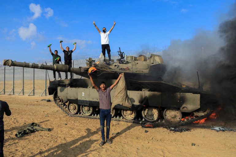 Palestinians celebrate as an Israeli military vehicle burns after it was hit by Palestinian gunmen who infiltrated areas of southern Israel, at the Israeli side of Israel-Gaza border, October 7, 2023. REUTERS/Yasser Qudih NO RESALES. NO ARCHIVES.