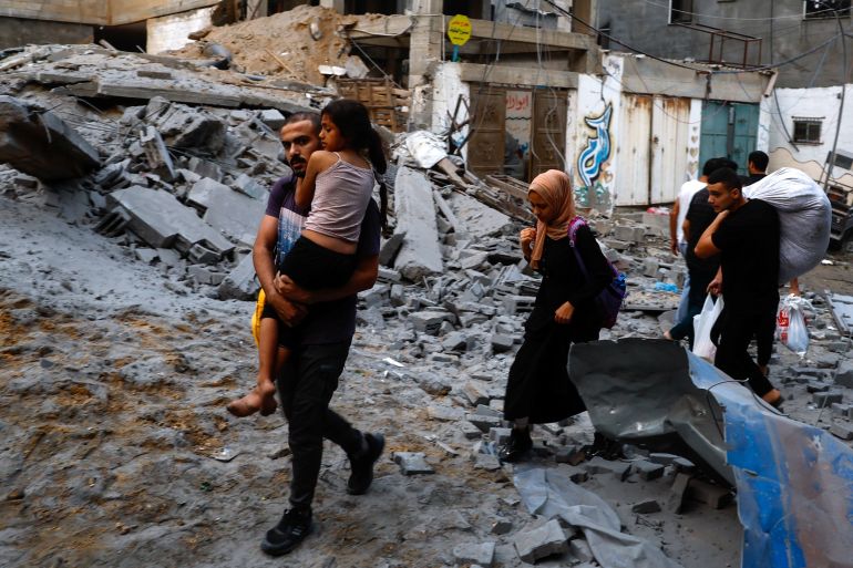 Palestinians carry their belongings as they walk on a debris-strewn street in the aftermath of Israeli strikes