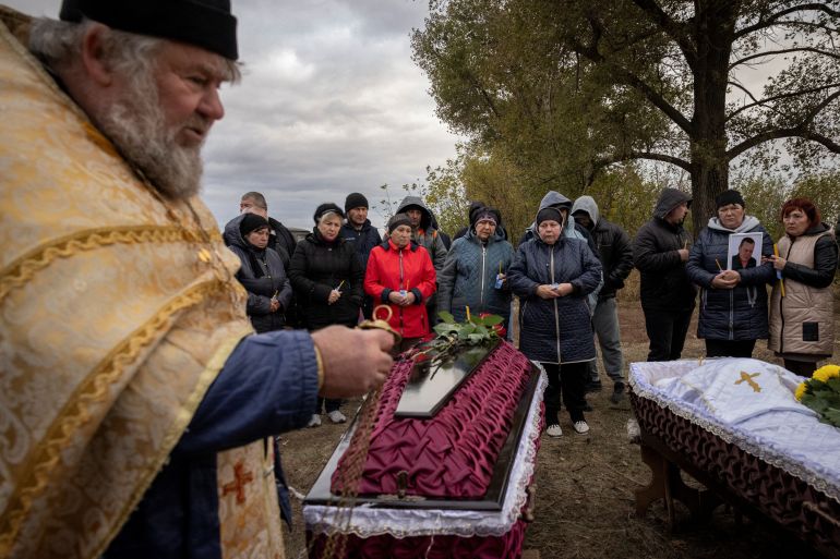 An Orthodox priest at a funeral for two of those killed in the missile attack on Hroza. Family members are behind. One is carrying a photograph of their loved one.