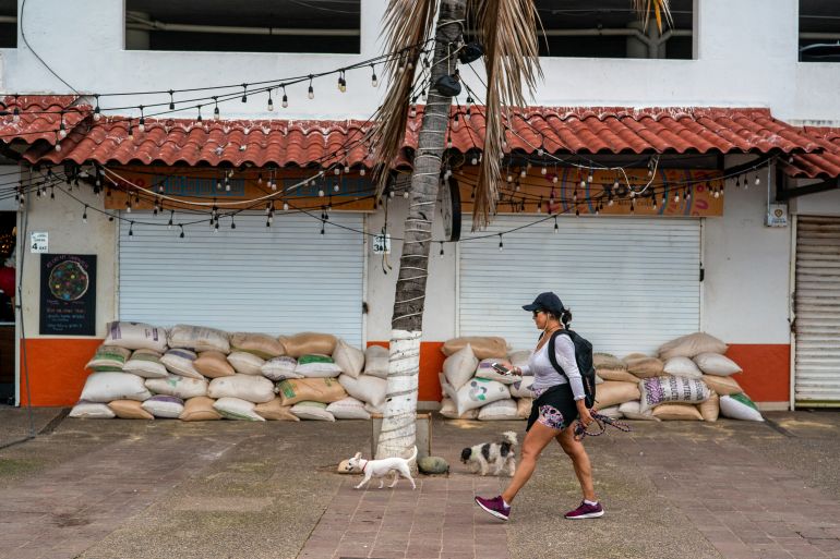 A woman walking her two dogs past a closed shop with sandbags piled against potential flooding