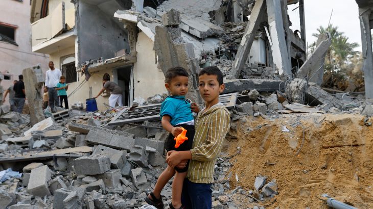 A Palestinian boy holds a child as he stands on the rubble of destroyed buildings