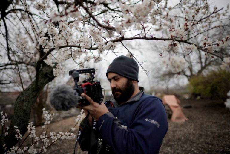 A man holding a video camera surrounded by a tree with blossoms