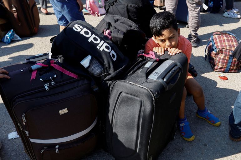 A small child seemingly cowers behind a black suitcase as his family waits along the southern Gaza border.