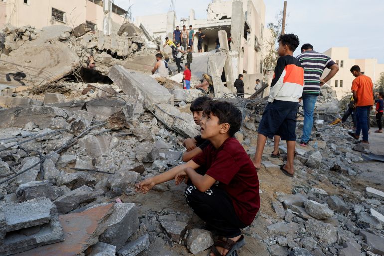 Palestinian children sit next destroyed building