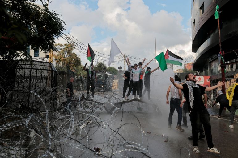 People hold flags among a cloud of tear gas while clashing with security forces during a protest in support of Palestinians, near the U.S. embassy in Awkar, after hundreds of Palestinians were killed in a blast at Al-Ahli hospital in Gaza that Israeli and Palestinian officials blamed on each other, Lebanon October 18, 2023
