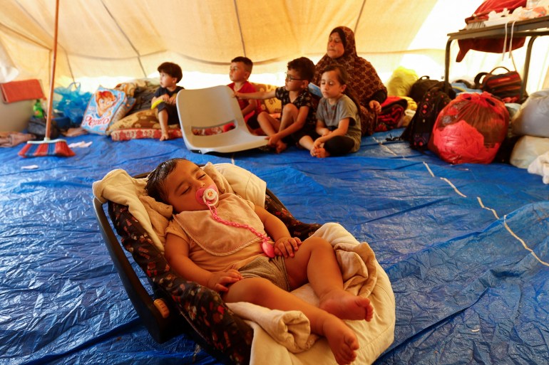 A woman sits with children in a tent, as Palestinians, who fled their houses amid Israeli strikes, take shelter in a tent camp at a United Nations-run centre, after Israel's call for more than 1 million civilians in northern Gaza to move south, in Khan Younis in the southern Gaza Strip,