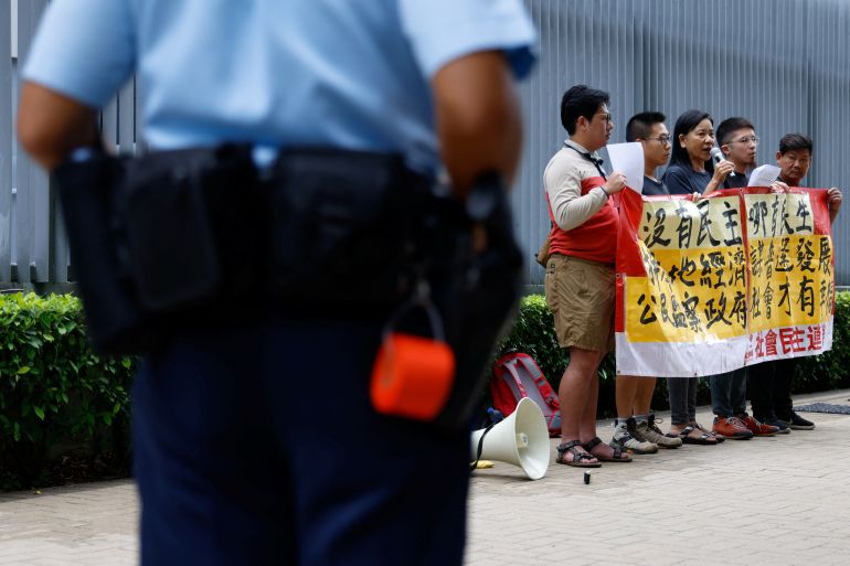 A police officer keeping watch on a protest by five people in Hong Kong. The group is demanding universal suffrage and has a large banner.