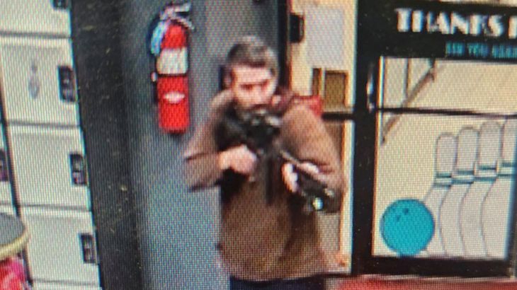 The photo of the suspect released by police. He is wearing a brown shirt and jeans an holding the rifle to his shoulder in a shooting position.