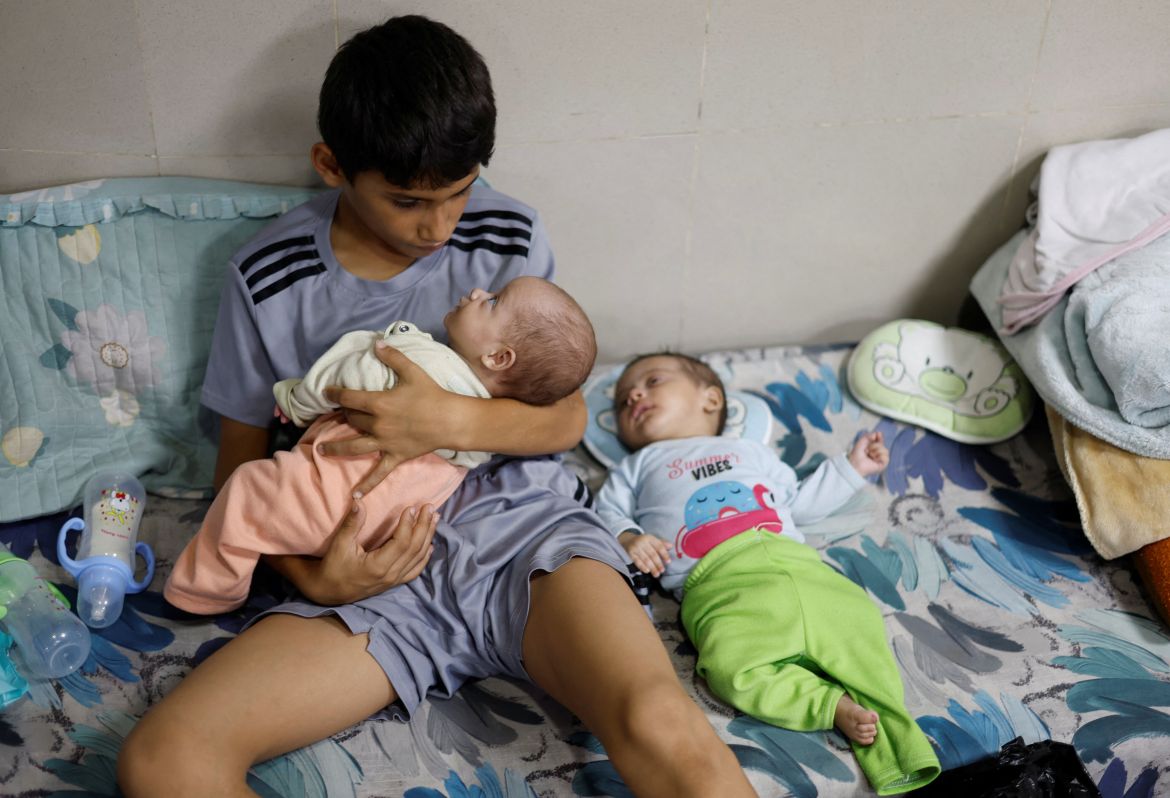 A displaced Palestinian boy, who fled with his family from their house amid Israeli strikes, looks after his twin siblings as they take shelter at Nasser hospital in Khan Younis in the southern Gaza Strip