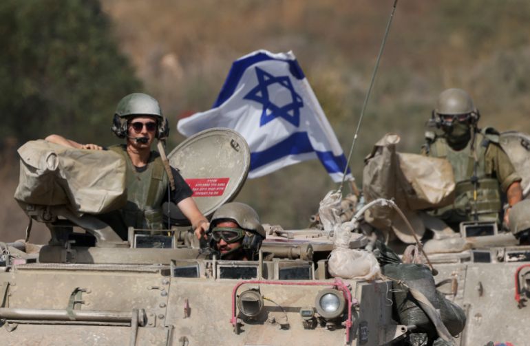Israeli soldiers in helmets and fatigues are seen atop an armoured vehicle carrying medical supplies, waving an Israeli flag.