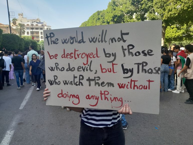 A protester in Tunis holds a handmade sign that says: “The world will not be destroyed by those who do evil, but by those who watch them and do nothing.”