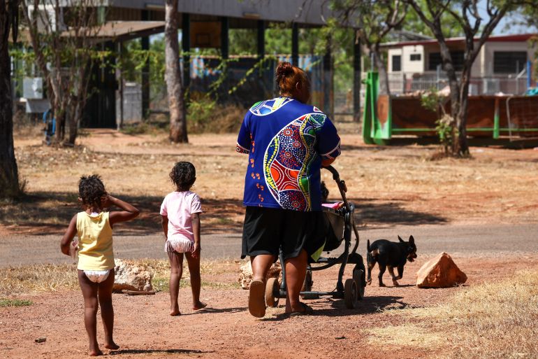 Am Aboriginal woman walking with two young children in a community in Australia's Northern Territory. She is pushing a push chair.