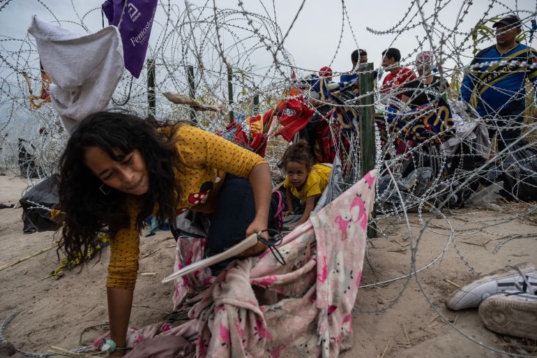 Migrants from Venezuela crawl through a hole in the razor wire to cross into Eagle Pass, Texas