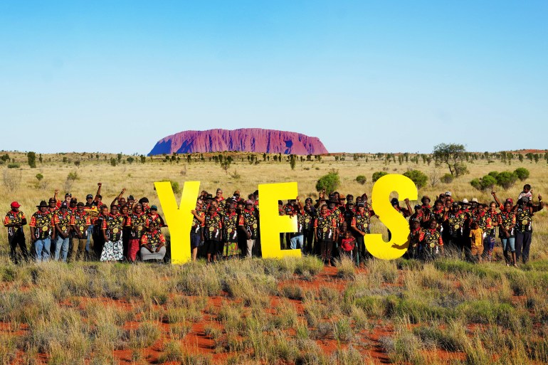 Yes voters gather in central Australia. Uluru is behind them. They are holding up the letters Y, E and S.