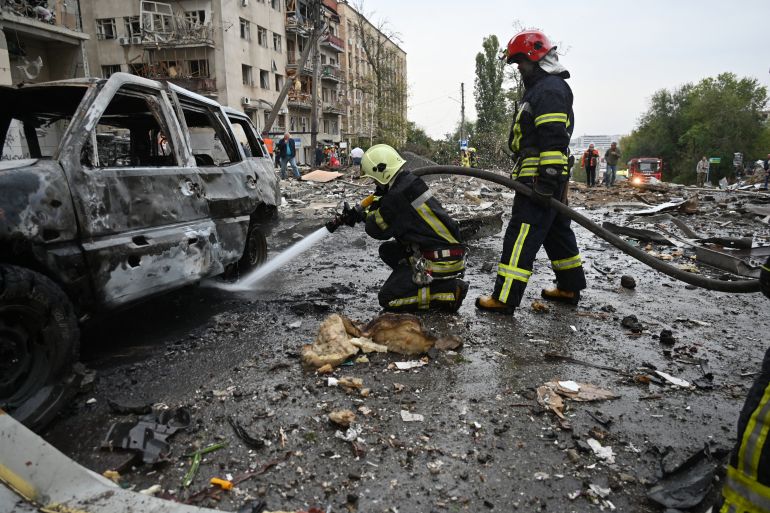 Firefighters use a water hose on a burning car after a Russian strike to the center of the Ukrainian city of Kharkiv on October 6, 2023, amid Russian invasion in Ukraine. - At least sixteen people were wounded and a child reported dead after a Russian strike on Kharkiv, said the Ukrainian Interior Minister. (Photo by SERGEY BOBOK / AFP)