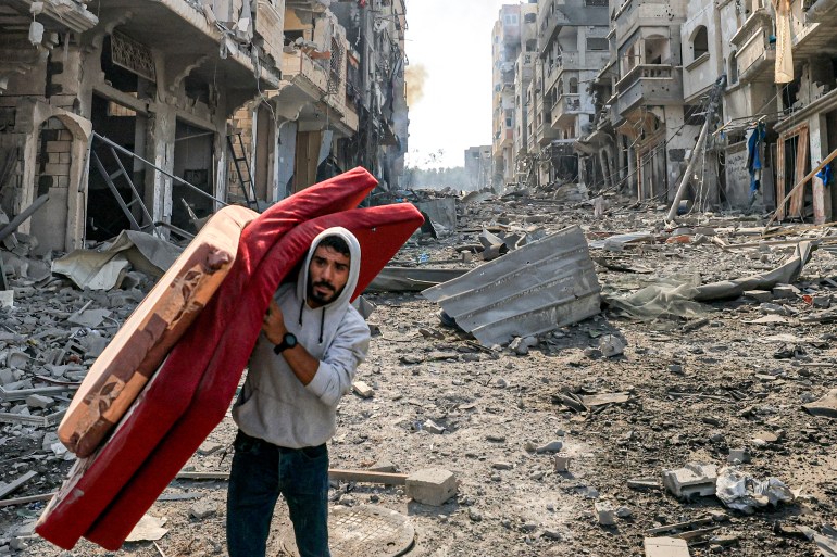 A man walks with mattresses through destruction in the Gaza Strip's