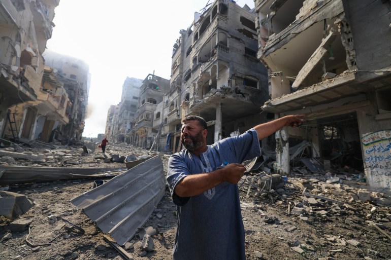 A Palestinian man points at destruction