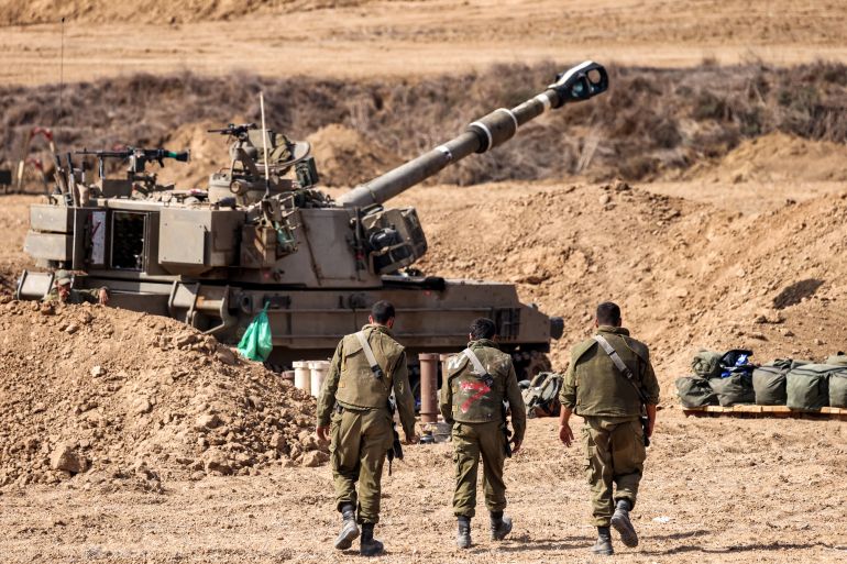 Israeli army soldiers walk near a self-propelled howitzer