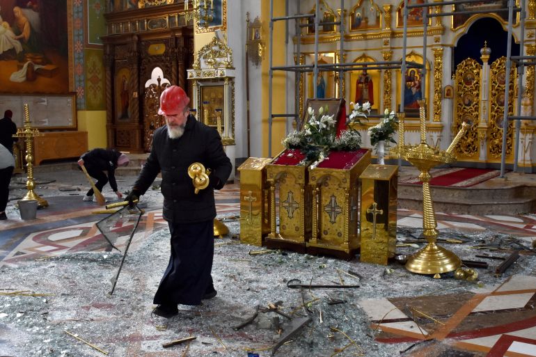 A priest cleans up debris in front of the altar after a missile attack on Zaporizhzhia
