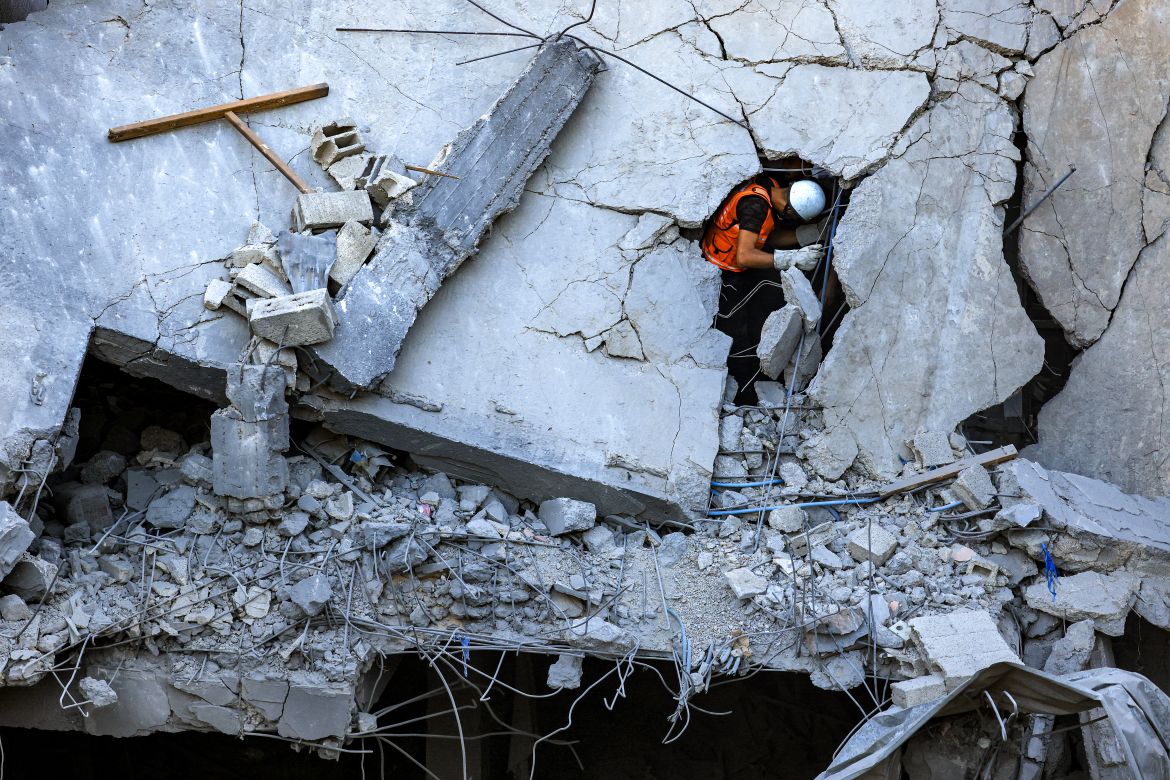 A Palestinian civil defence member stands through a crack in a collapsed building hit by Israeli bombardment while searching for victims and survivors, in Khan Yunis