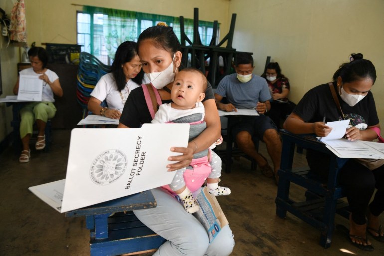 A mother holding her child goes through voting documents at a polling station for the nationwide village and youth elections in Manila