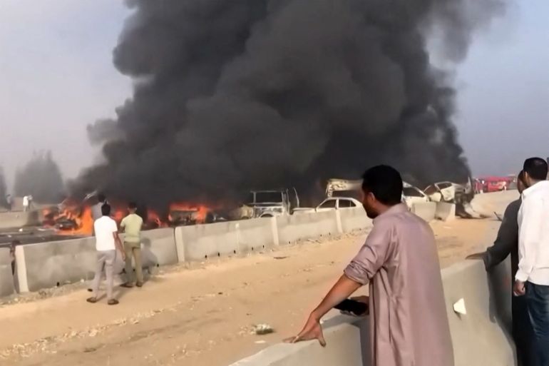 A grab from a UGC video posted on Facebook on October 28, 2023, shows people watching as black smoke billows from charred vehicles following a collision on the Cairo-Alexandria desert road near Wadi al-Natrun that reportedly left at least 35 people dead and more than 50 people dead. - Traffic accidents are common in Egypt where roads are often in bad repair and the highway code is frequently disregarded. (Photo by -UGC / UGC / AFP) / RESTRICTED TO EDITORIAL USE  MANDATORY CREDIT « AFP PHOTO / UGC VIA FACEBOOK» - NO MARKETING NO ADVERTISING CAMPAIGNS NO RESALE  DISTRIBUTED AS A SERVICE TO CLIENTS - RESTRICTED TO EDITORIAL USE  MANDATORY CREDIT « AFP PHOTO / UGC via Facebook» - NO MARKETING NO ADVERTISING CAMPAIGNS NO RESALE  DISTRIBUTED AS A SERVICE TO CLIENTS /