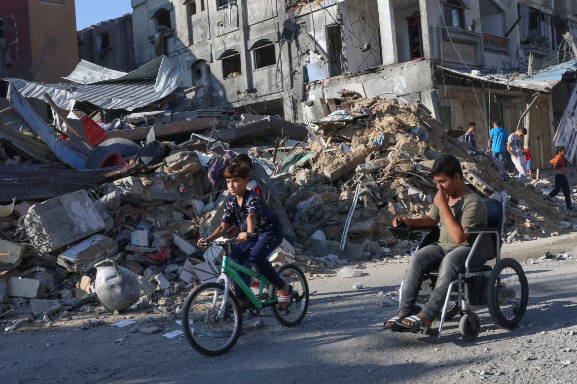 Palestinian boys one on a bicycle the other in a wheelchair pass by building rubble