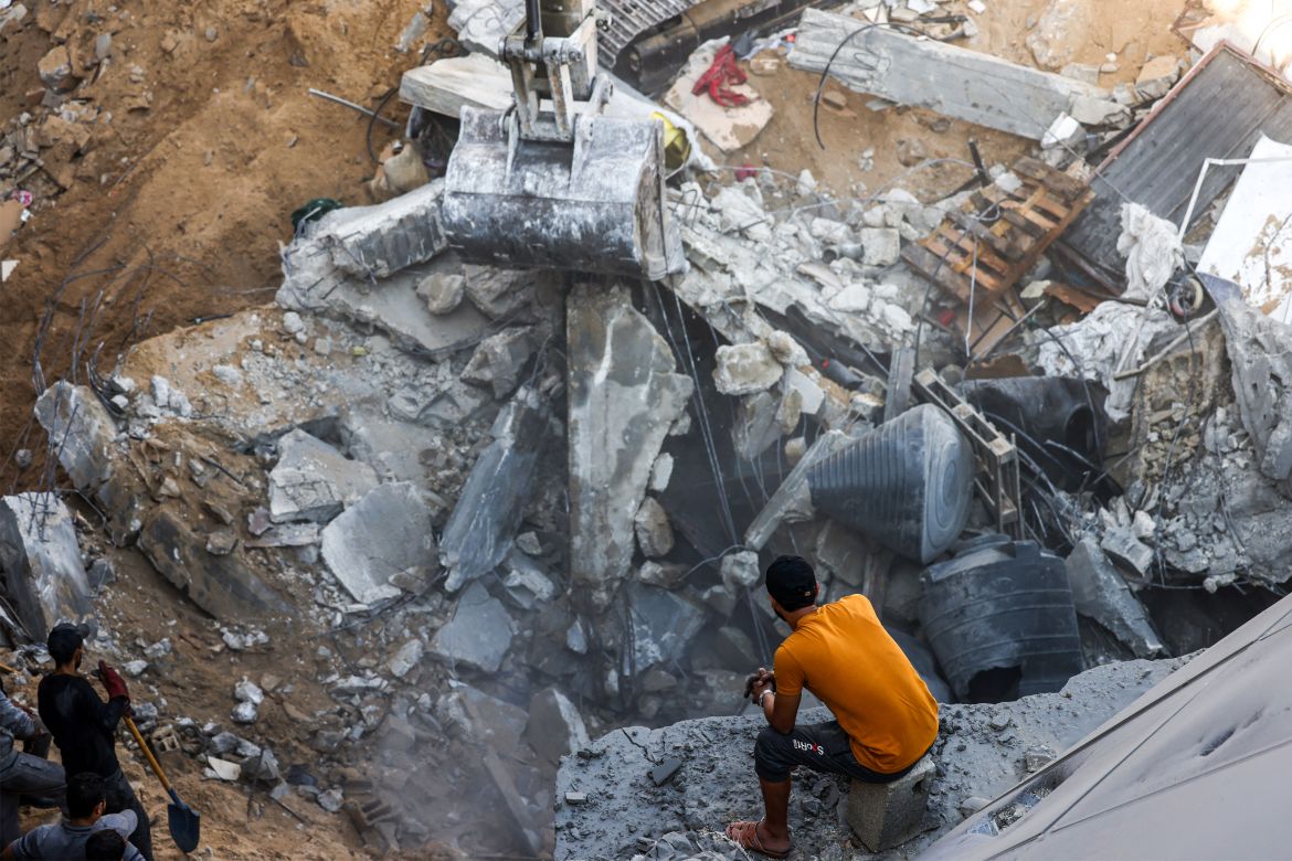 A man looks on as an excavator clears rubble after a building was hit by Israeli bombardment in Rafah