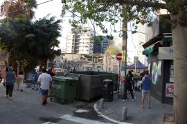 A crew clears rubble from a building hit in Tel Aviv as curious citizens gather