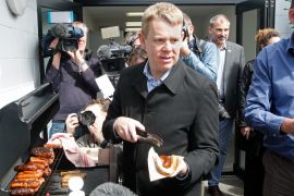 Chris Hipkins putting a sausage in a bun at a barbecue. Photographers are around him.