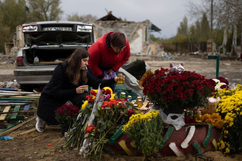 Two women laying flowers and lighting candles for the victims of a Russian rocket attack in the village of Hroza