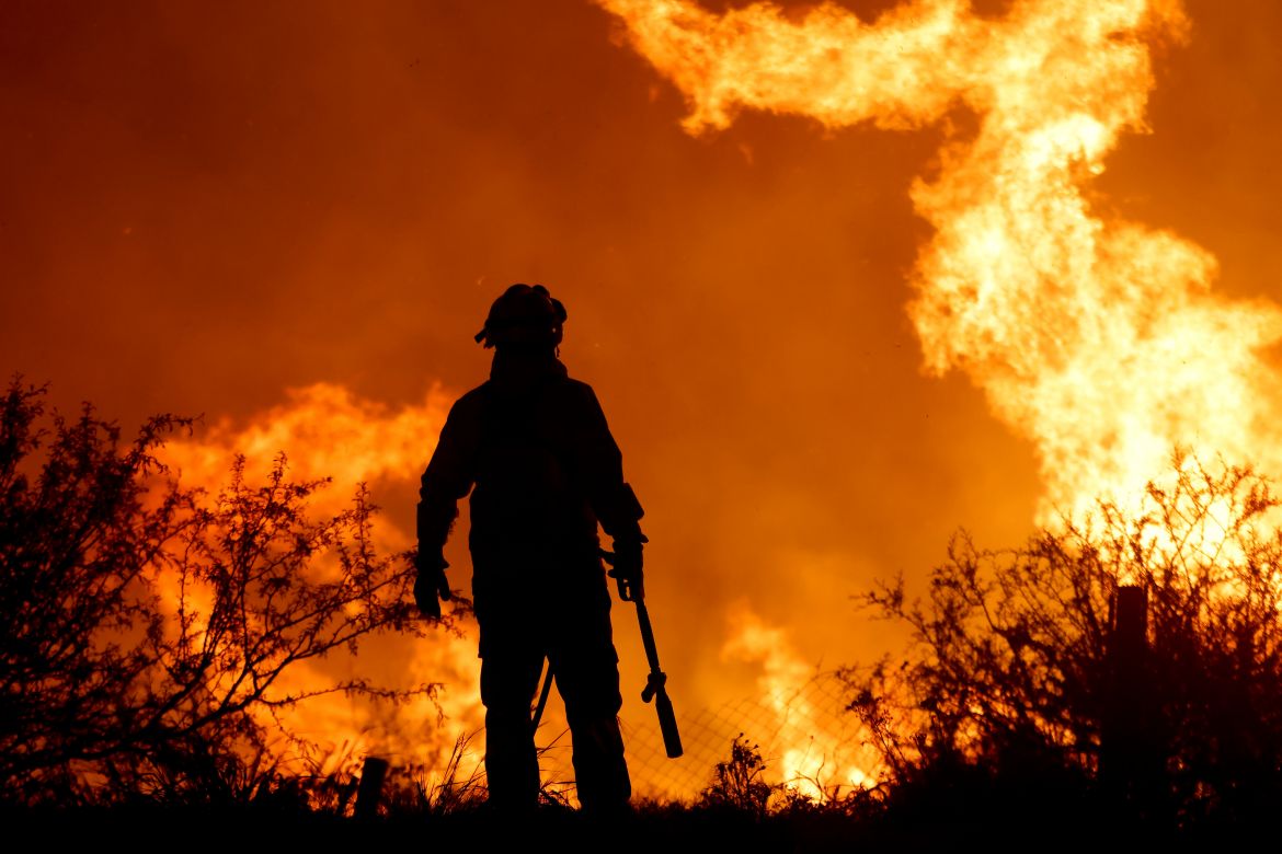 A firefighter is silhouetted by the flames of a forest fire on the outskirts of Villa Carlos Paz, Argentina