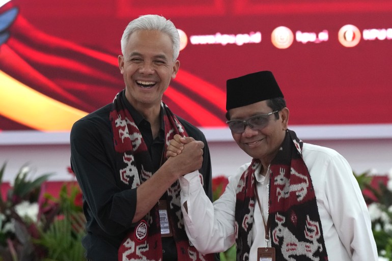 Presidential candidate Ganjar Pranowo (left) shakes hands with his running mate Mahfud MD. They are both smiling.