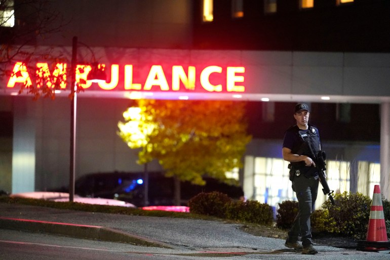 An armed police officer outside the Central Maine Medical Center. The word AMBULANCE is lit up in red.