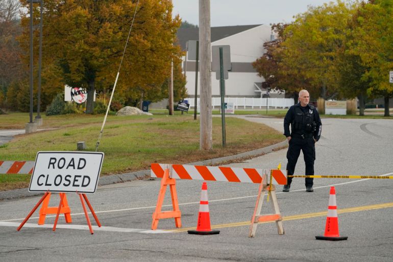 A police officer stands next to a sign saying 'road closed'