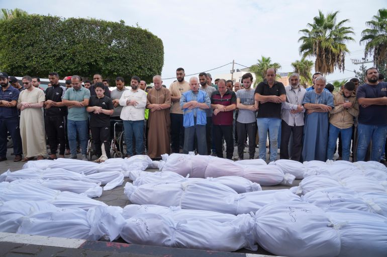 Palestinians pray for loved ones who lie in rows of body bags in Gaza